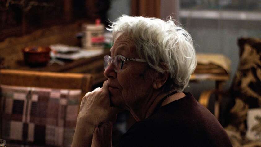 An image of an elderly woman sitting at a table with her face in her hands.