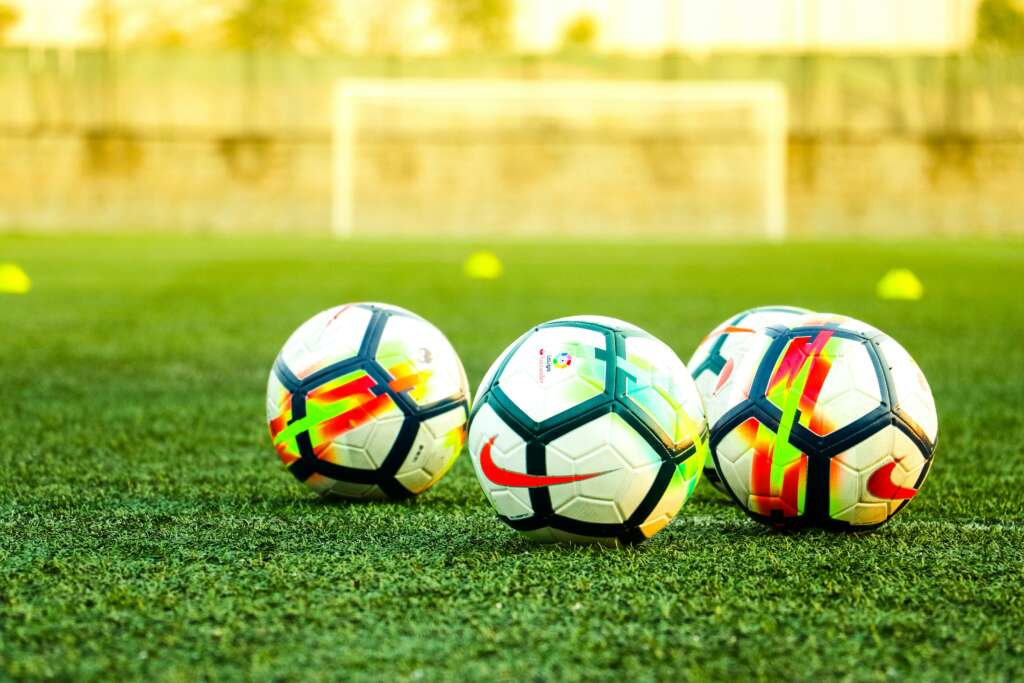 An image of a few different soccer balls on a turf field. 