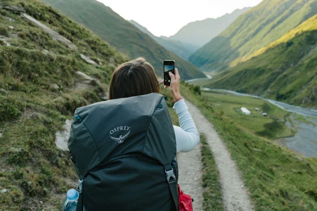 An image of a young woman taking a picture while hiking with her Osprey backpack on. 