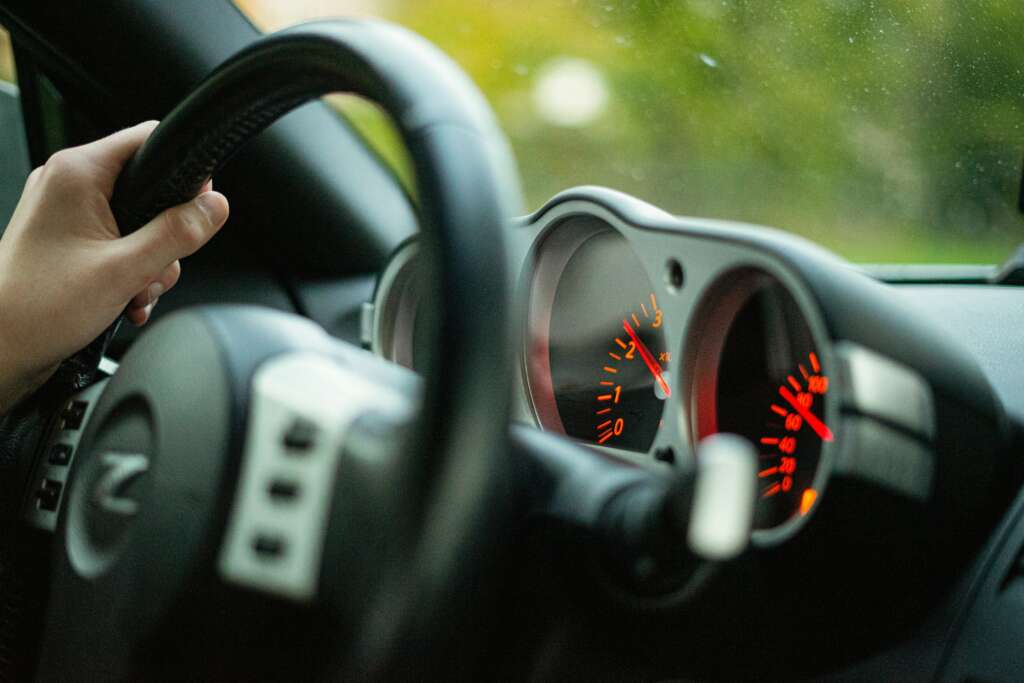 A close-up image of someone driving a car that shows part of the speedometer and fuel gauge. 