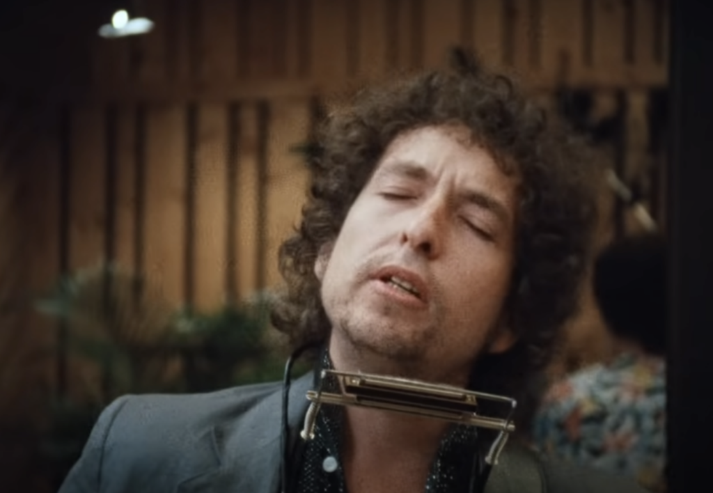 An image of Bob Dylan using a harmonica in a music video. 