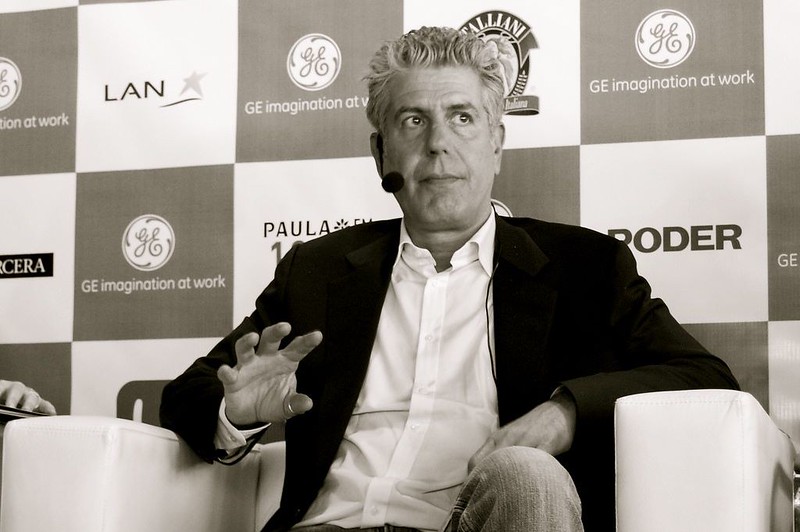 An image of Anthony Bourdain giving a speech with a microphone. 