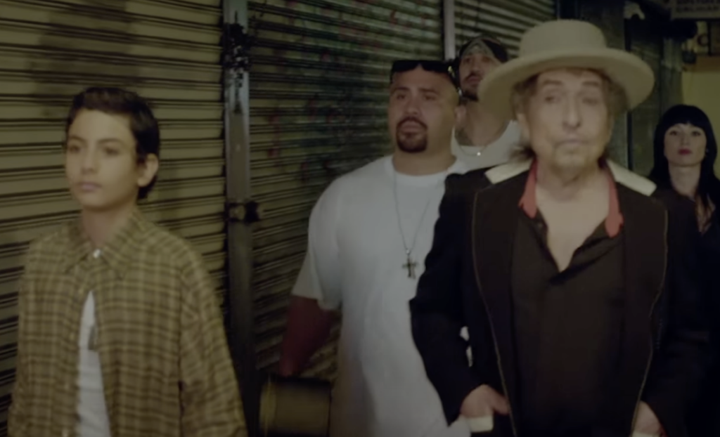 A still image of Bob Dylan walking in a group in one of his music videos. 