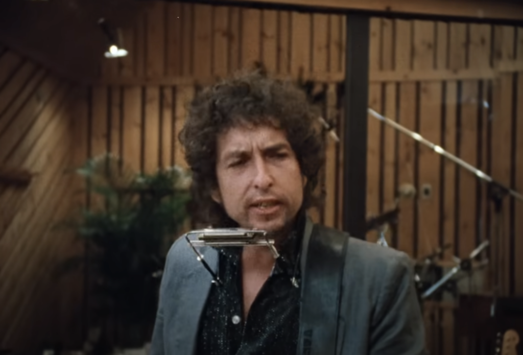 An image of Bob Dylan using a harmonica in a music video. 