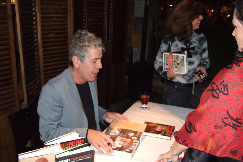 An image of Anthony Bourdain reading a menu at a restaurant. 