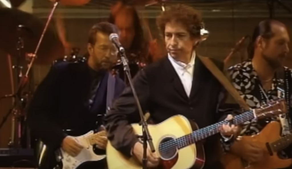 An image of Bob Dylan with his guitar on stage. 