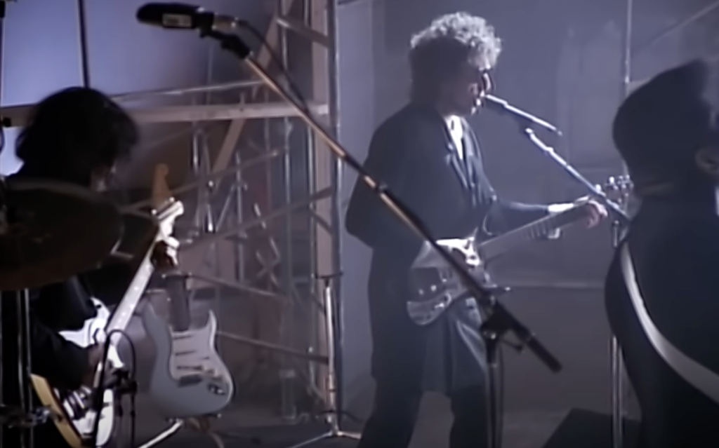 An image of Bob Dylan singing with sunglasses on. 