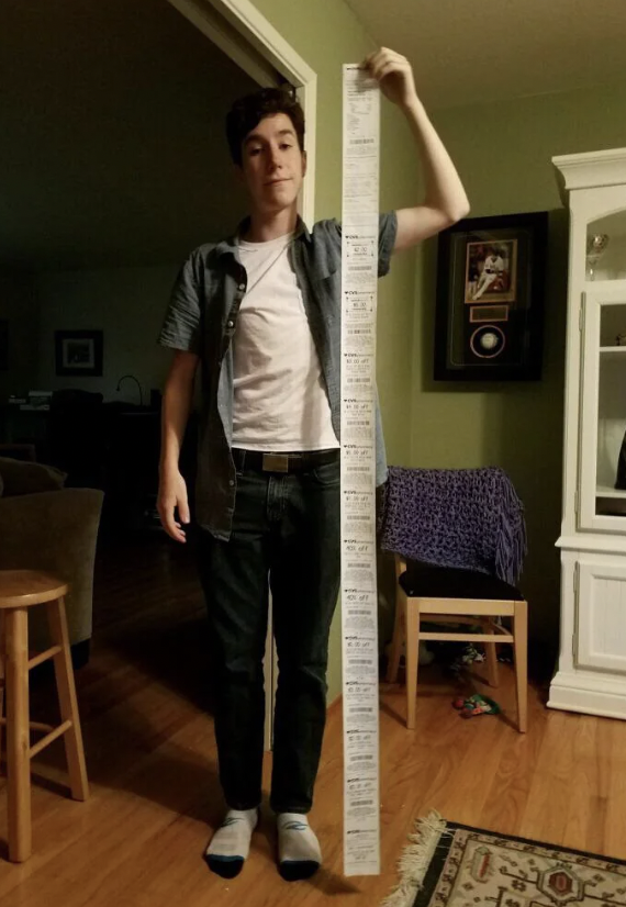 A young man holding up a huge receipt. 