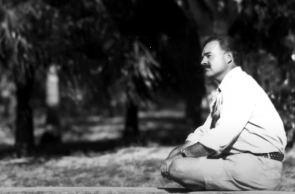 An image of Ernest Hemingway sitting cross-legged. 