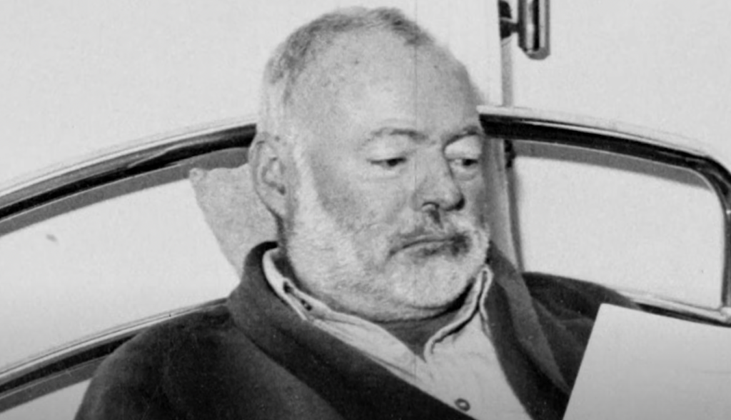 Older Ernest Hemingway reads his book in bed. 