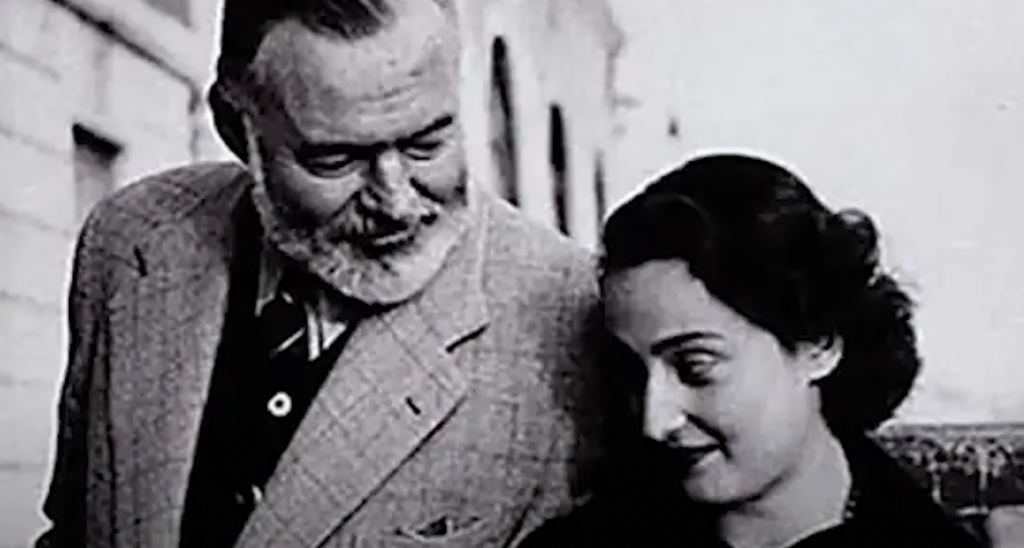 An older Ernest Hemingway looks at younger woman. 