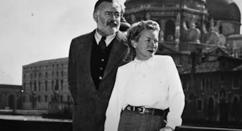 Ernest Hemingway stands next to a young woman. 