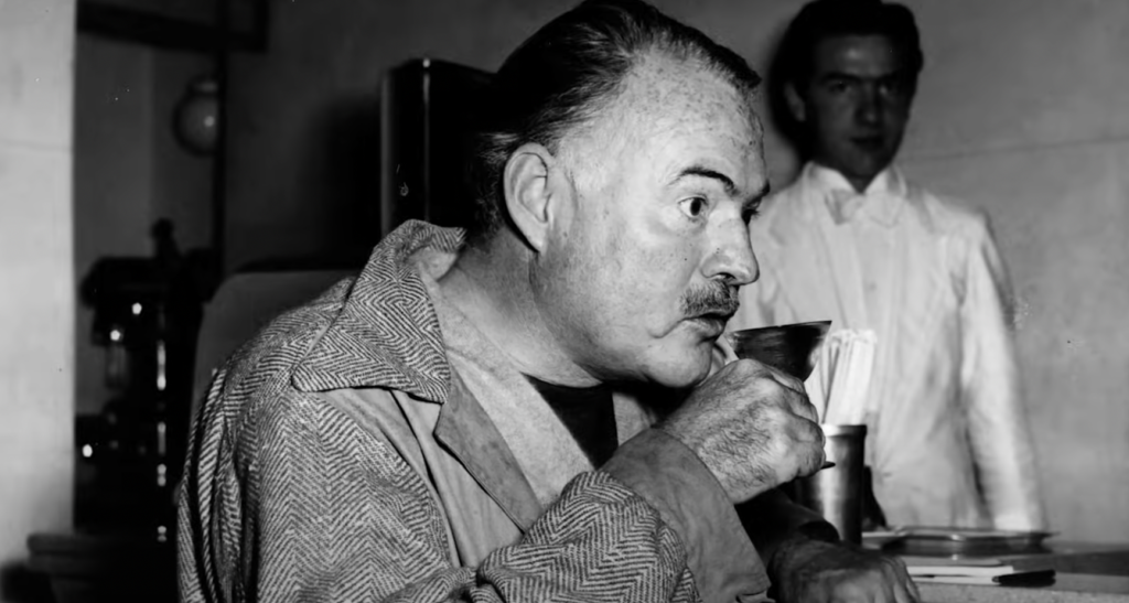 Ernest Hemingway sips from a glass. 