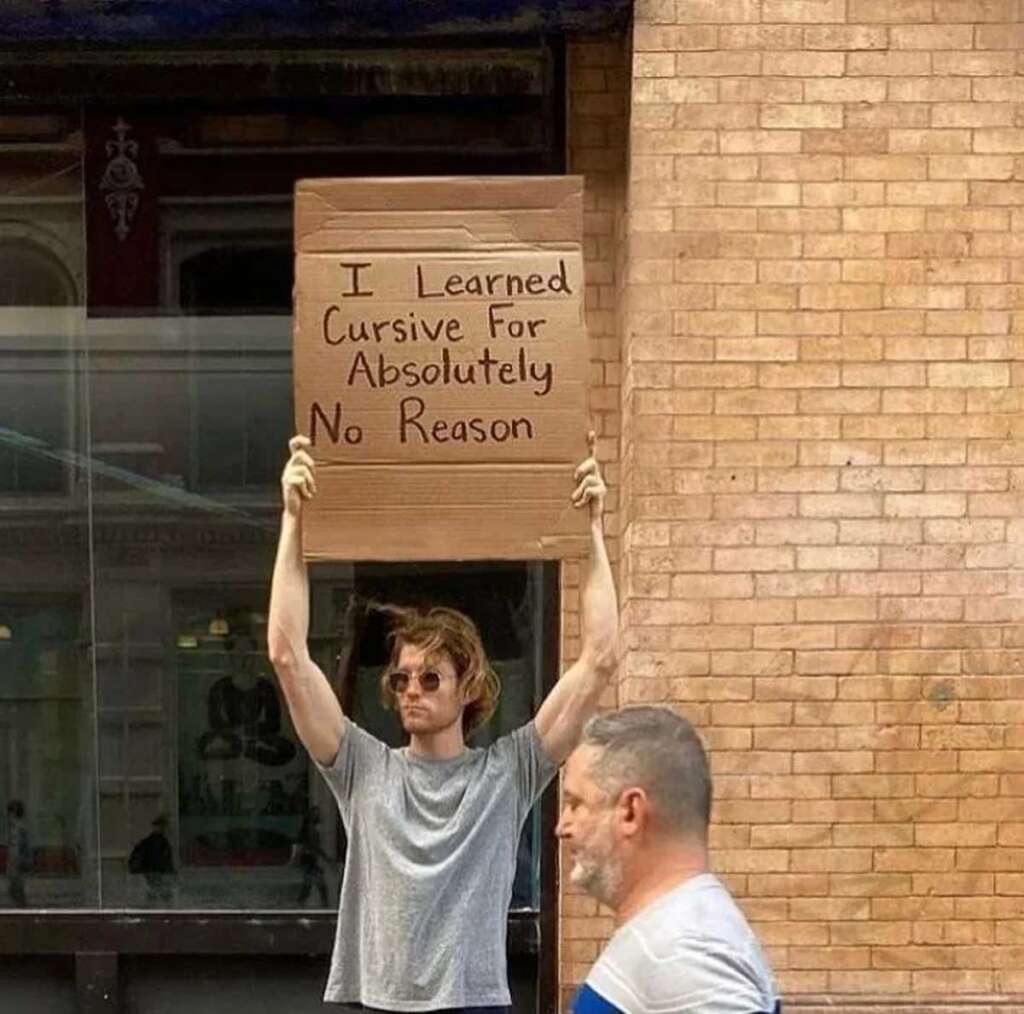 Man holding a sign that says "I learned cursive for absolutely no reason" 