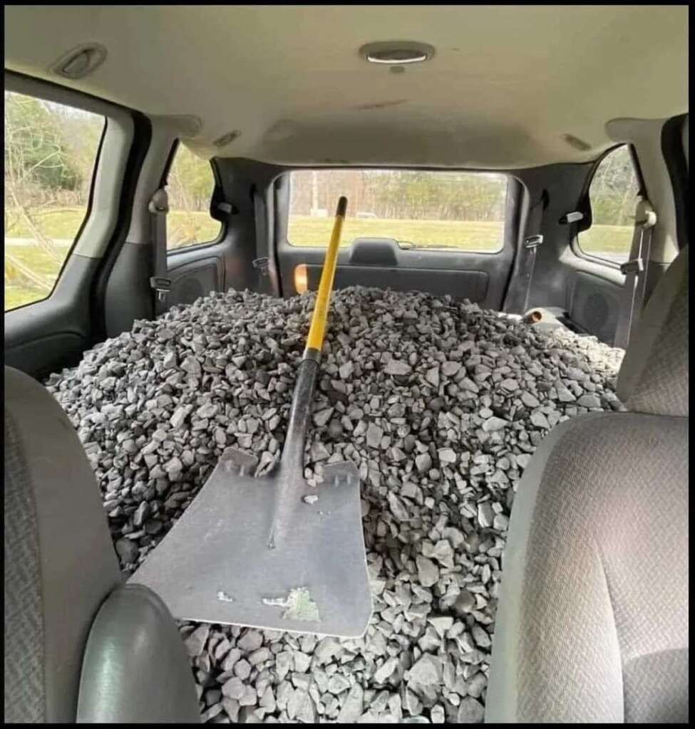 An SUV with the back filled with small rocks and a shovel