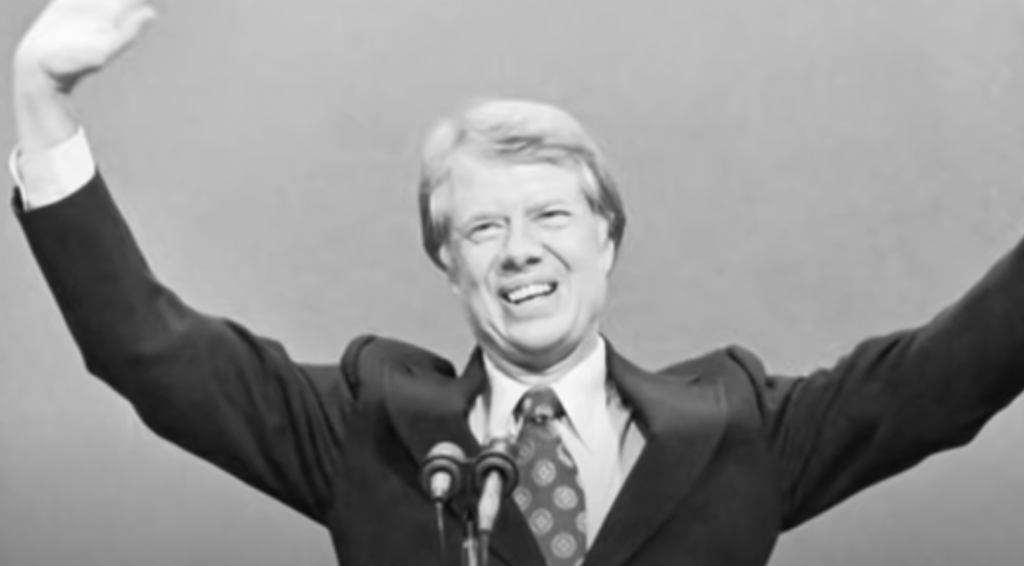 An image of Jimmy Carter smiling with hands over his head. 