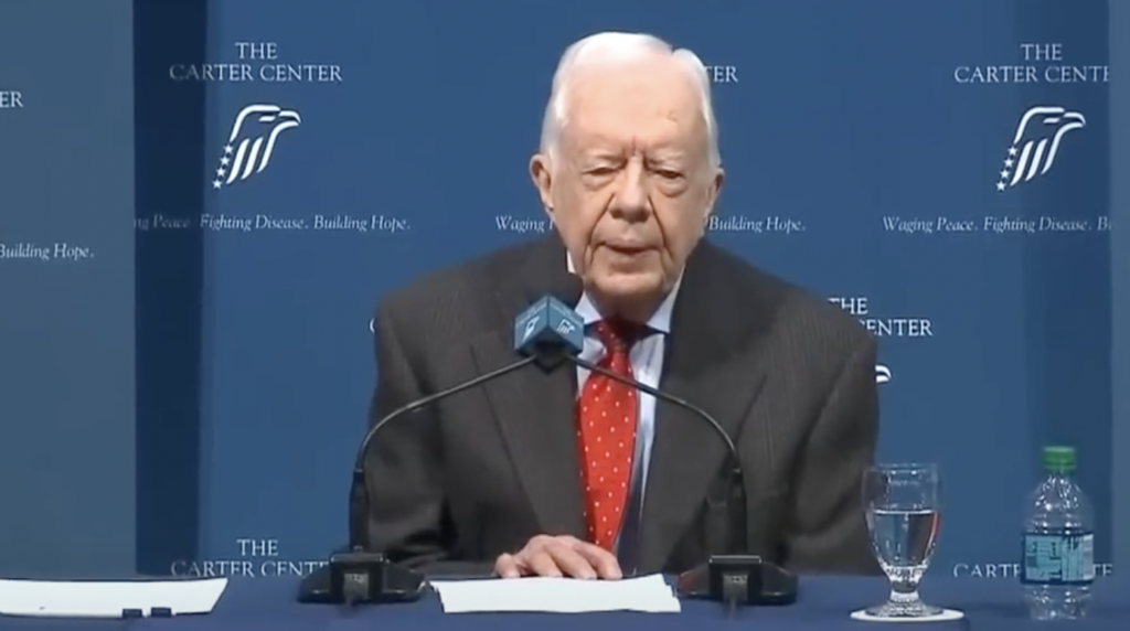 An image of an older Jimmy Carter giving a conference. 