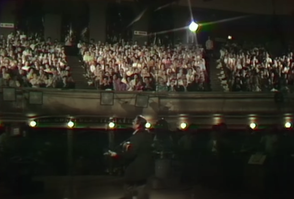A zoomed out shot of Johnny Cash singing to the crowd. 