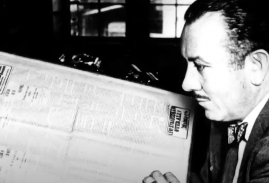 Black and white photo of John Steinbeck looking at old newspaper with mustache. 