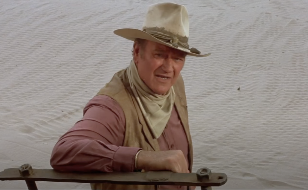 A still image of John Wayne talking seriously. 