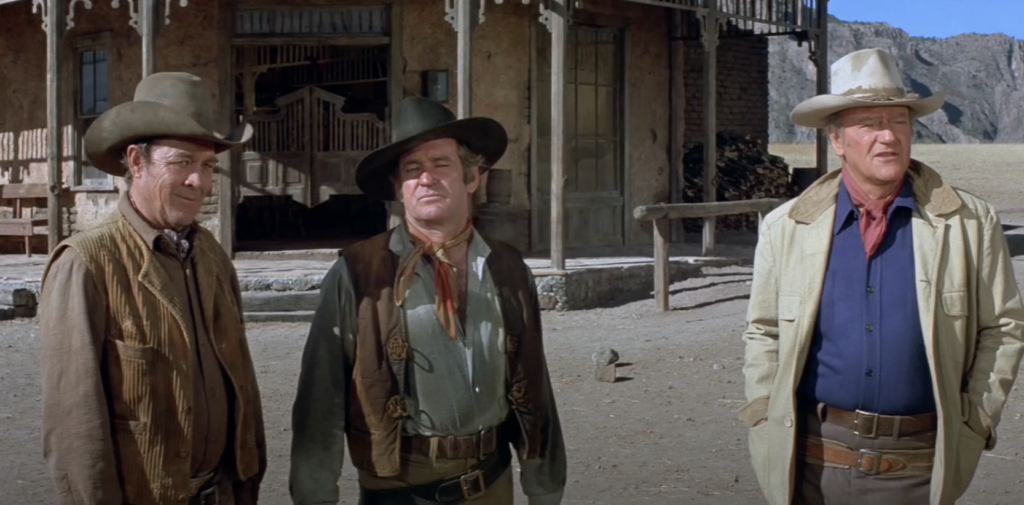 A still image of John Wayne next to a couple other cowboys. 