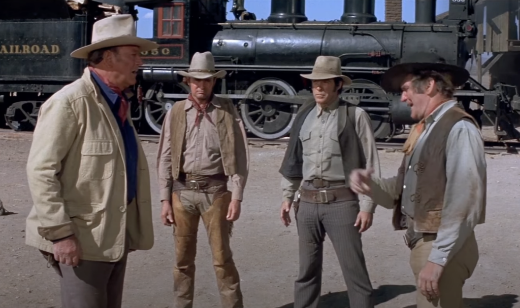 A still image of John Wayne talking to other western characters. 