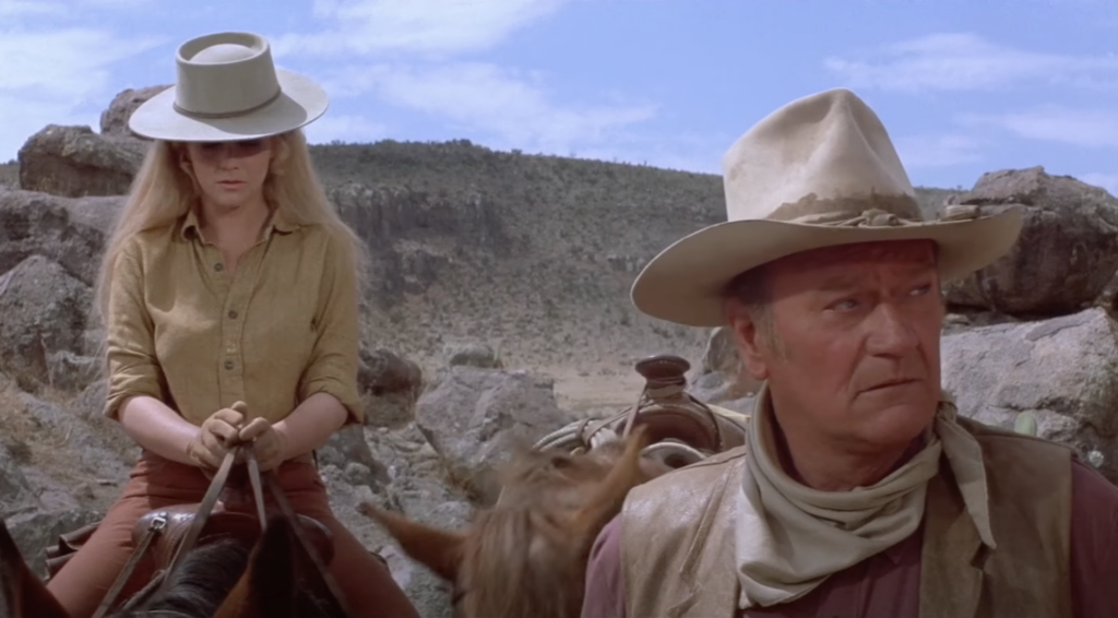 A still image of John Wayne next to a female on a horse. 