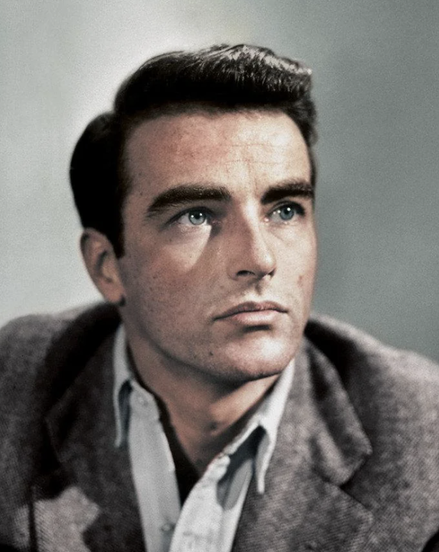 A man with dark hair gazes upward, wearing a gray suit jacket over a light-colored shirt. He appears contemplative, set against a neutral gray background.