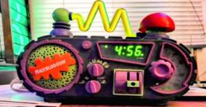 A colorful, retro-style alarm clock with a Nickelodeon logo. It features vibrant green, purple, and red accents, a wavy yellow antenna, and digital display showing 4:56. The design resembles a playful, fictional radio transmitter.