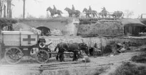 A historical scene shows a horse-drawn medical vehicle marked with a red cross near sandbagged structures. Soldiers on horseback ride across a bridge above. The area appears to be a war zone with rugged terrain and construction.