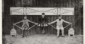 Three men in vintage clothing demonstrate the strength of a bridge design: two sit on chairs with bricks suspended by rods, while the third is seated between them, supported by the rods, with a bridge diagram behind them.