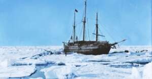 A wooden sailing ship is trapped in thick sea ice under a clear blue sky, surrounded by snow and icy water in a polar landscape.