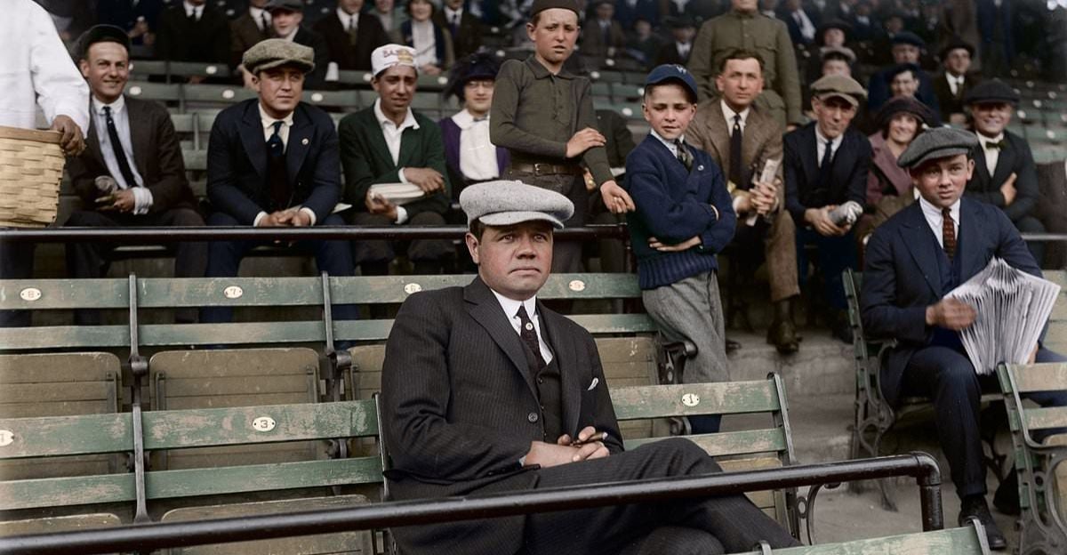 A man in a suit and flat cap sits alone in a row of empty stadium seats, while a group of people, mostly men and boys in early 20th-century attire, watch from behind him.