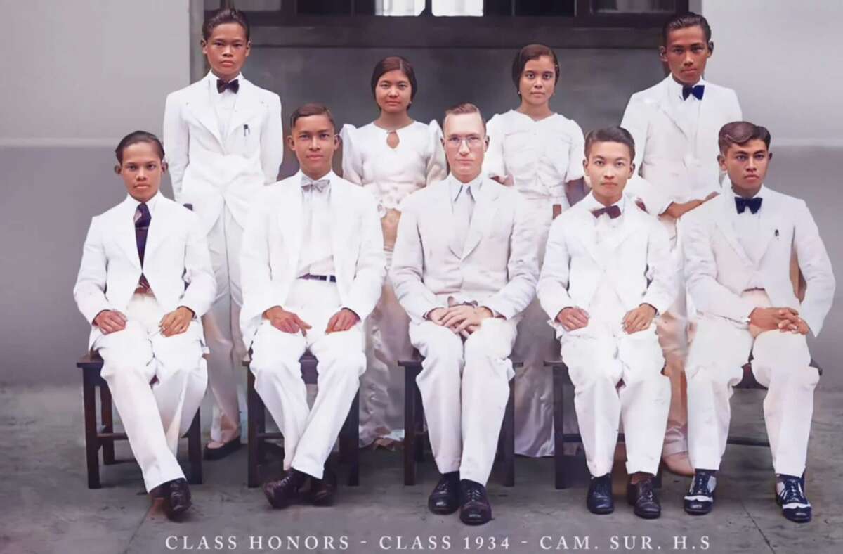 A formal group portrait of eight students and one teacher in white suits and dresses, seated and standing in two rows, with the text "Class Honors - Class 1934 - Cam. Sur. H.S." at the bottom.