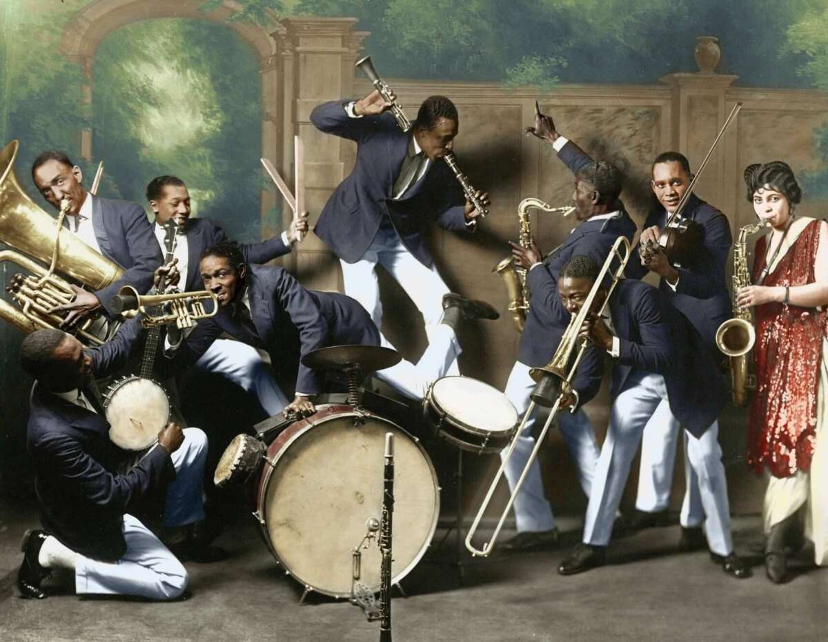A lively jazz band in blue suits plays various instruments, including drums, trumpet, clarinet, trombone, and saxophone, as a woman in a red dress stands singing beside them. The background is a painted garden scene.