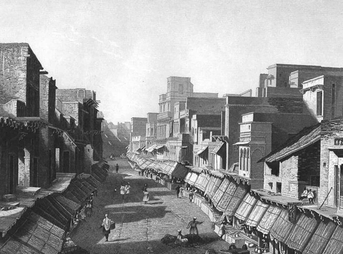 A black-and-white illustration of a wide street in an old city, lined with buildings and shops with awnings. People walk along the street and sit by the roadside. The scene appears historical and bustling.