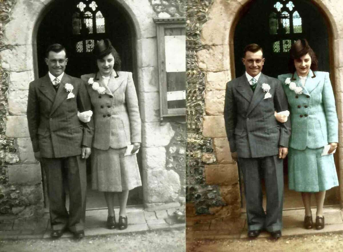 Two people dressed in vintage suits stand side by side in front of a stone arched doorway. The left half of the image is in sepia tones, while the right half is colorized, showing the woman’s suit in teal and the man’s in grey.