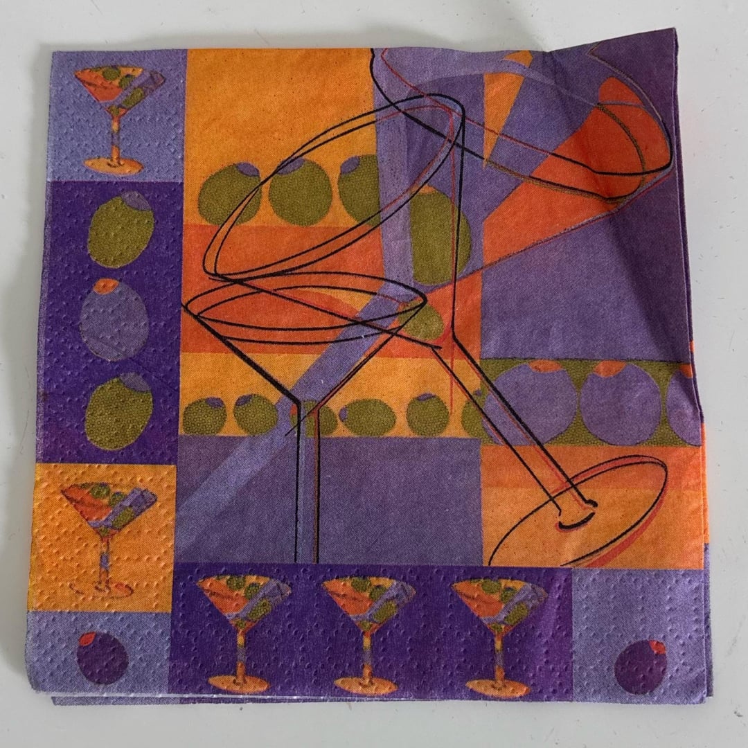 A colorful napkin features abstract martini glasses and olives in orange, purple, and green blocks and patterns.