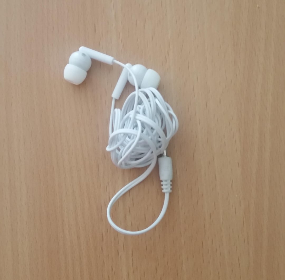 A pair of white wired earphones with tangled cords and white silicone ear tips resting on a light wooden surface.