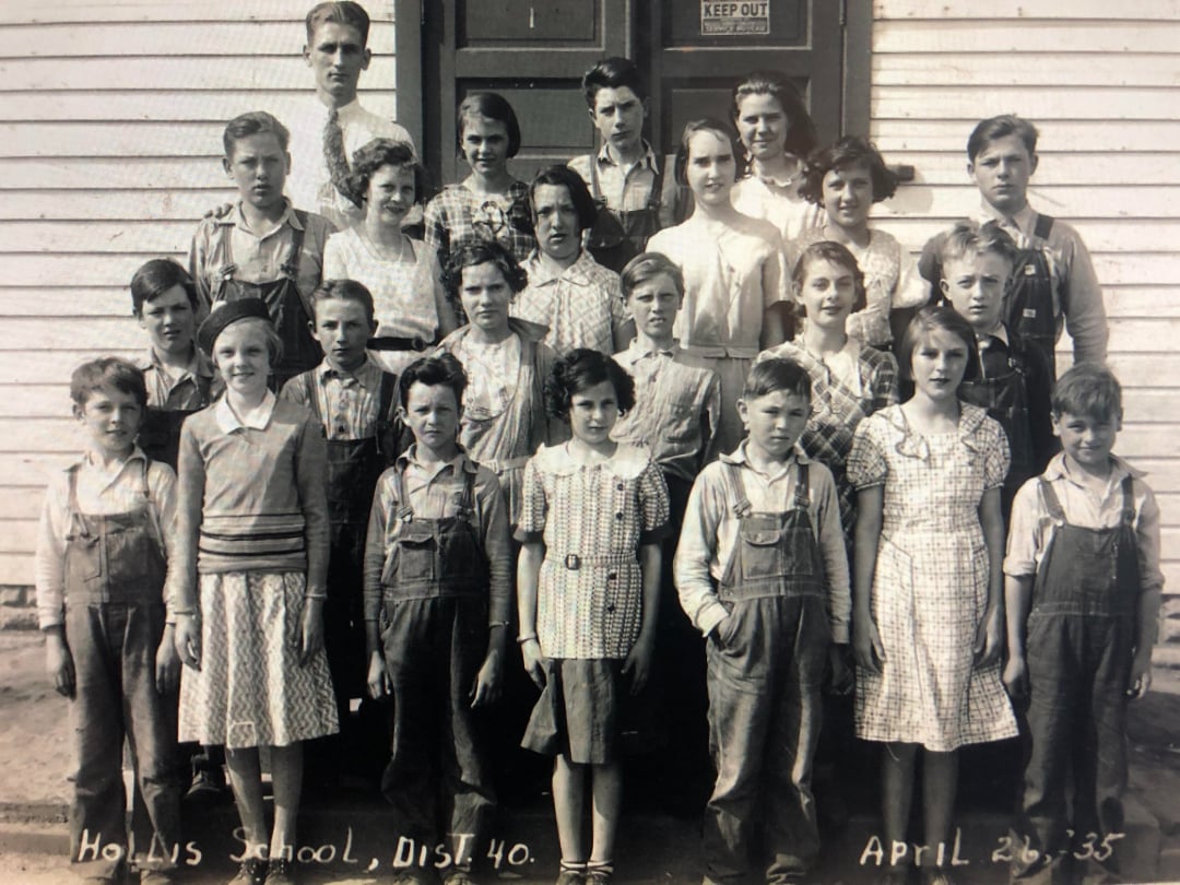 A black and white photo of 24 children and one adult, posing in front of a school building. They wear 1930s clothing. The sign reads "Hollins School, Dist. 40" with the date April 26, 1935.