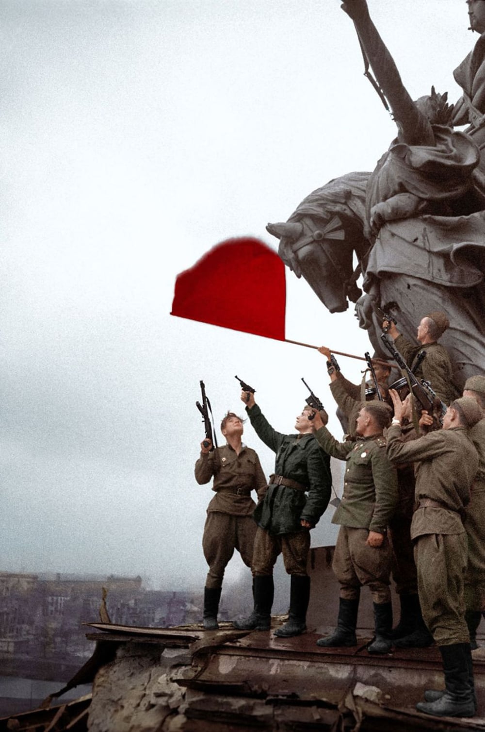 A group of soldiers stands on a damaged building rooftop, raising a red flag beside a large statue. The sky is overcast and city ruins are visible in the background.