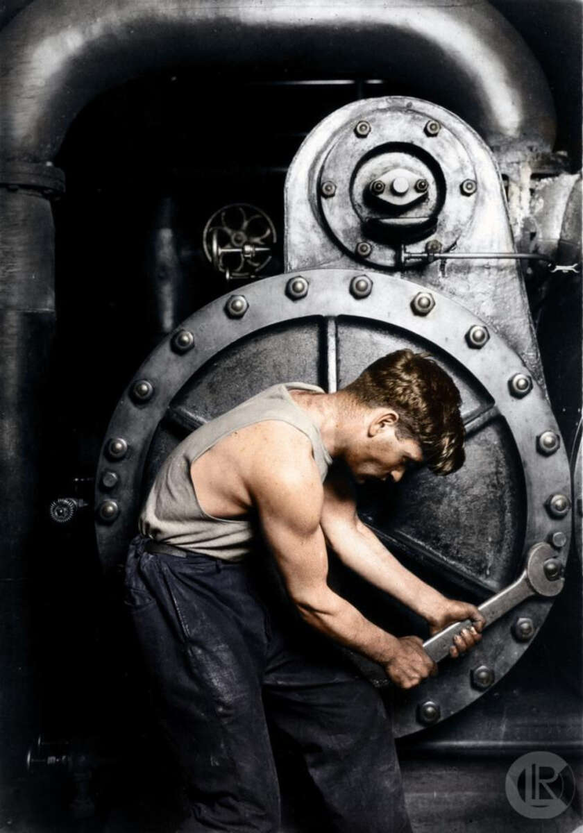 A man in a sleeveless shirt uses a large wrench to tighten bolts on industrial machinery, highlighting his muscular arms amid a backdrop of metal pipes and gears.
