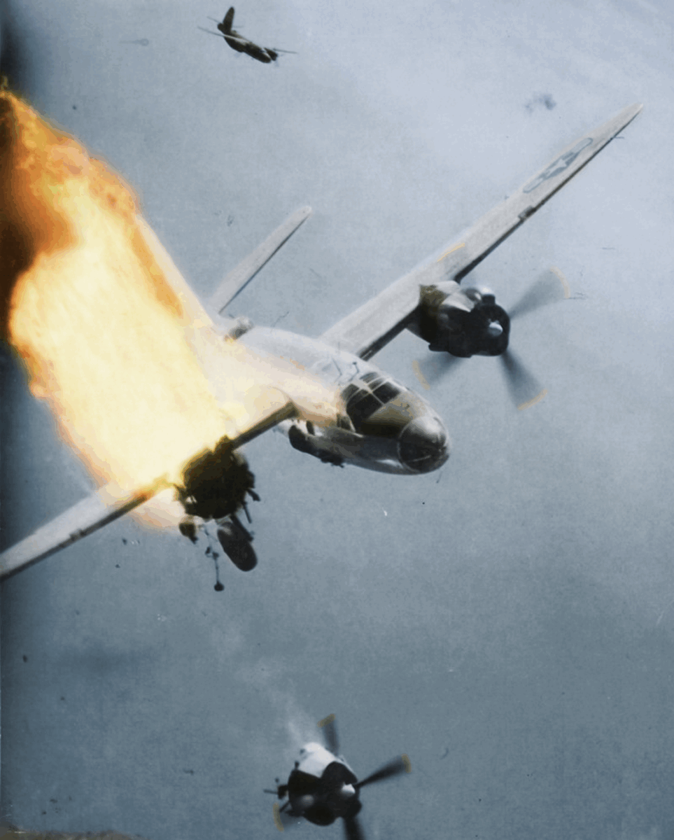 A World War II-era bomber aircraft is engulfed in flames on one engine while losing altitude, with parts falling off and another plane flying above in the background.