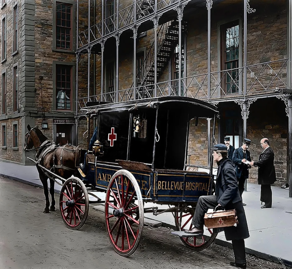 A vintage horse-drawn ambulance carriage with “Bellevue Hospital” written on the side is parked outside a brick building. A doctor holding a medical bag approaches, while two men converse near the entrance.