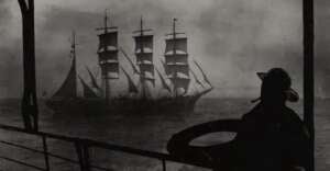 A silhouette of a person stands on a ship&rsquo;s deck, looking out at a large, old-fashioned sailing ship with multiple masts on the open sea, shrouded in mist.