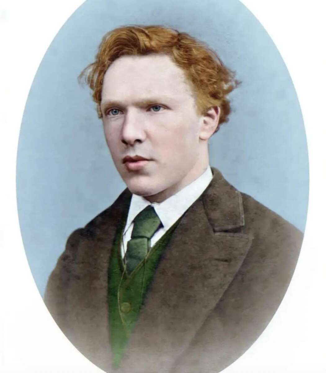 A colorized portrait of a young man with wavy red hair, fair skin, and blue eyes, wearing a brown jacket, white shirt, green vest, and green tie, set against a pale blue background.