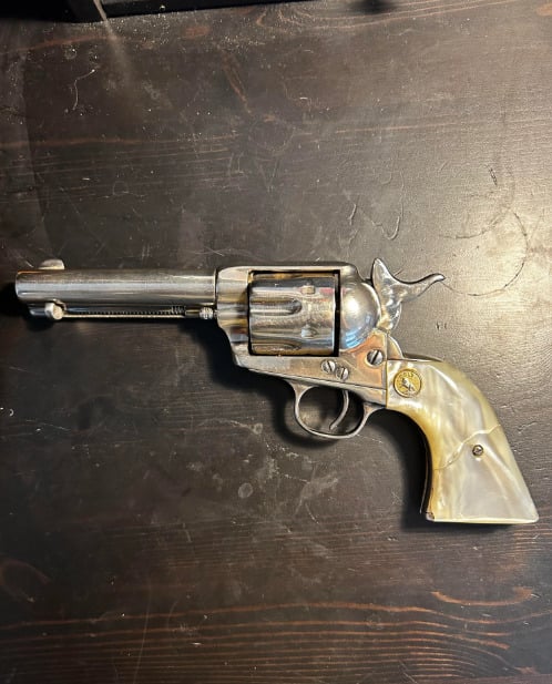 A silver revolver with an ornate, shiny ivory-colored handle is displayed on a dark wooden surface.