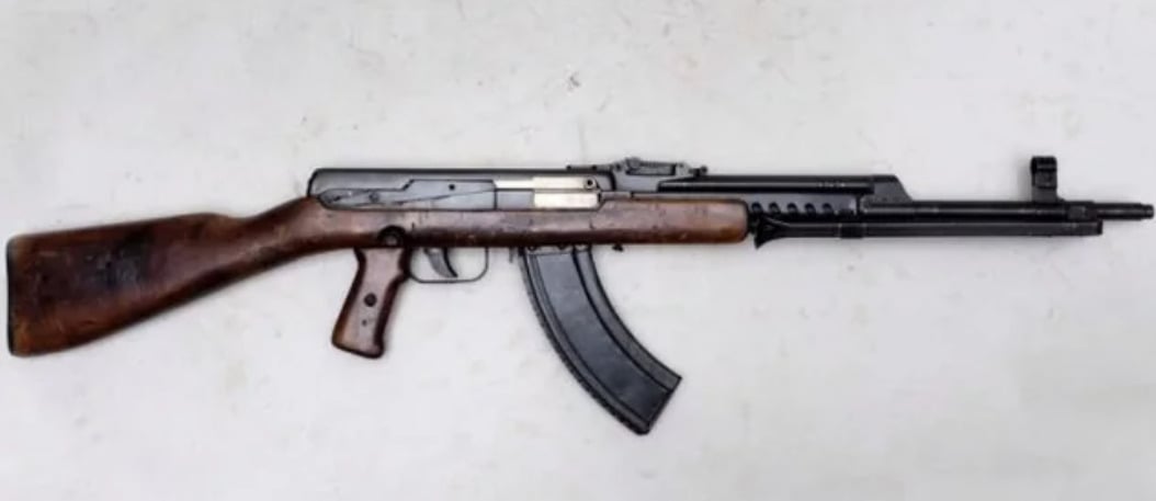A vintage assault rifle with a wooden stock and grip, a black metal body, and a curved magazine, displayed on a light background.