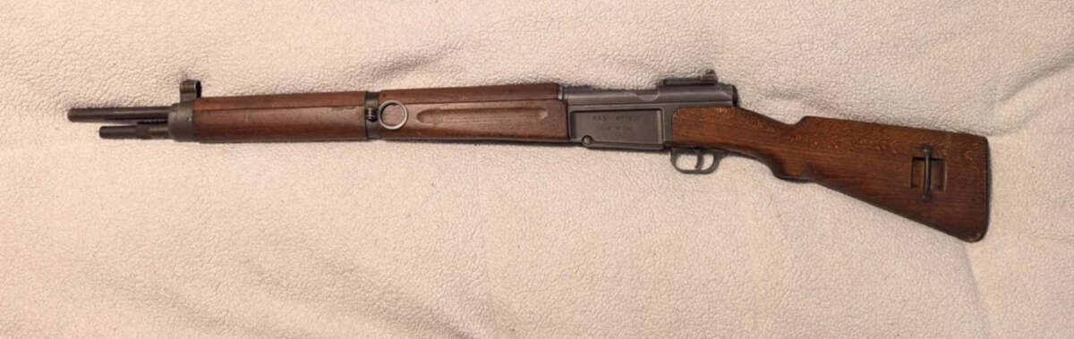 A vintage military rifle with a wooden stock and metal barrel is displayed on a light-colored textured surface.