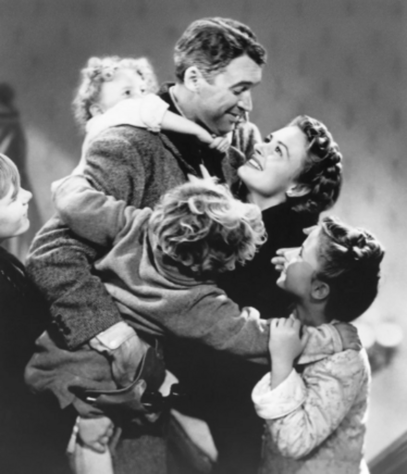 A joyful family hugs closely, with a man and woman at the center smiling at each other, surrounded by happy children in an affectionate, black-and-white scene.